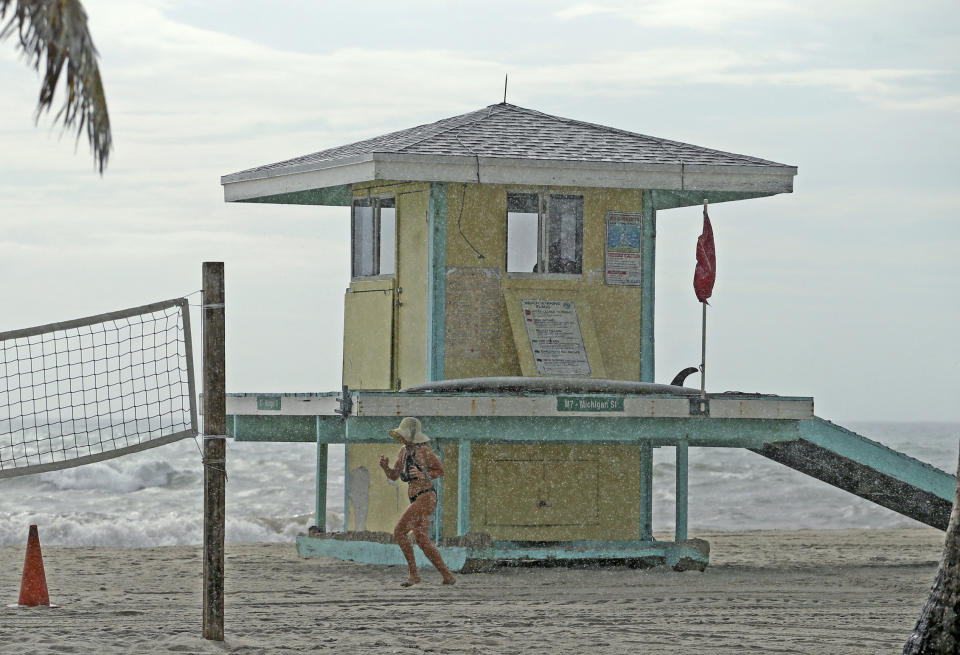 A beachgoer runs under the rain at the beach on Saturday, Aug. 31, 2019 at Hollywood, Fla. The latest forecast says Hurricane Dorian is expected to stay just off shore of Florida and skirt the coast of Georgia, with the possibility of landfall still a threat on Wednesday, and then continuing up to South Carolina early Thursday. (David Santiago/Miami Herald via AP)