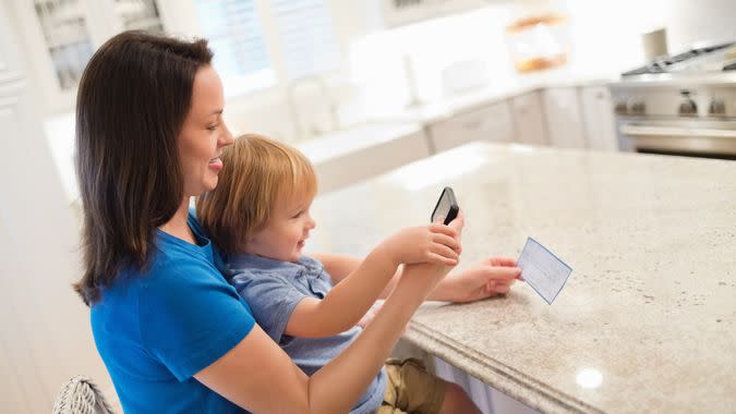 Side view of mother and son depositing check through smart phone in kitchen.