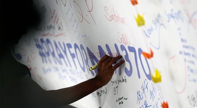 A man writes messages and well wishes on a banner dedicated to all involved with the missing Malaysia Airlines jetliner MH370 on the walls of the Kuala Lumpur International Airport. Photo: AP.