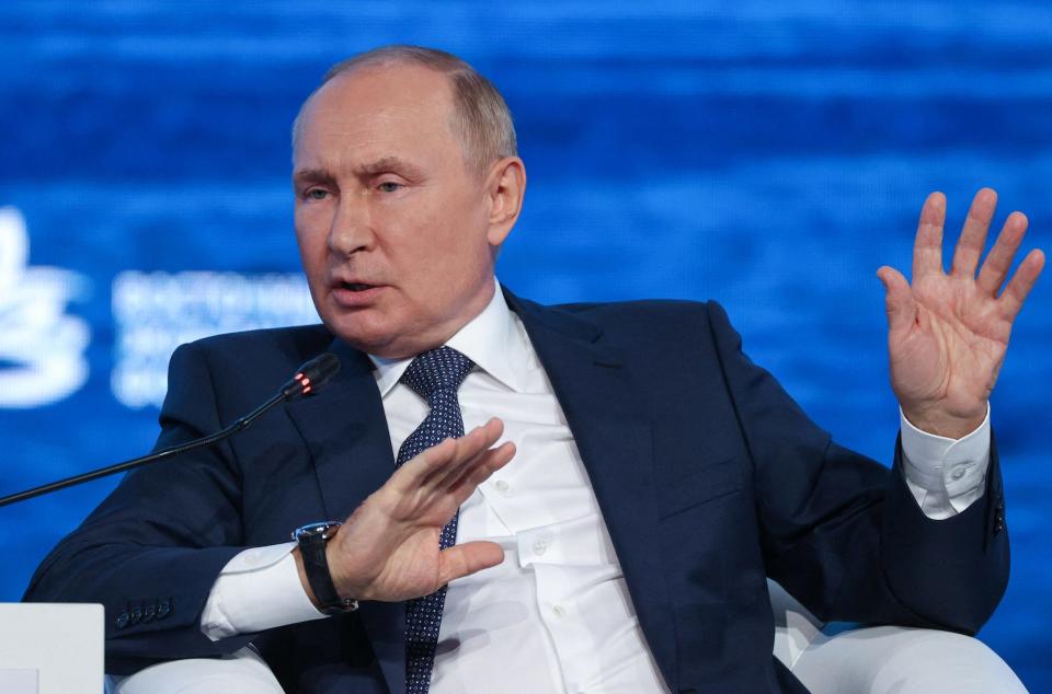 Russian President Vladimir Putin gestures in a suit with a blue background behind him