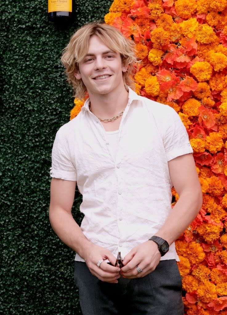 Ross Lynch smiling and standing against a backdrop of flowers