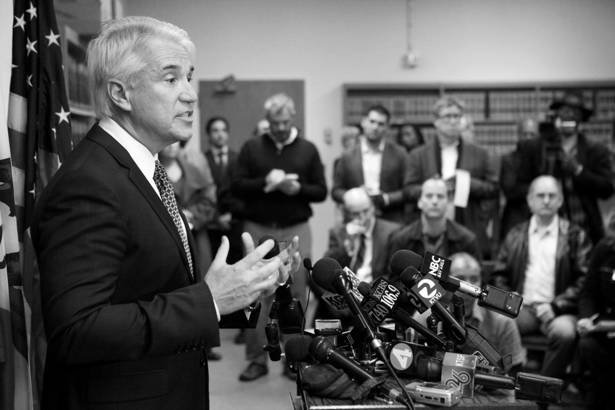 George Gascón stands before a podium with multiple microphones.