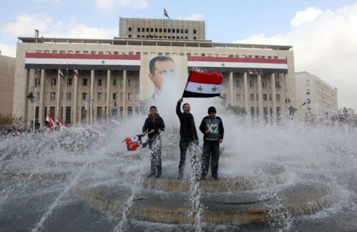 Syrian government supporters wave national flags they stand in a fountain in front of a portrait of President Bashar al-Assad during a pro-regime rally in Damascus on January 26, 2012