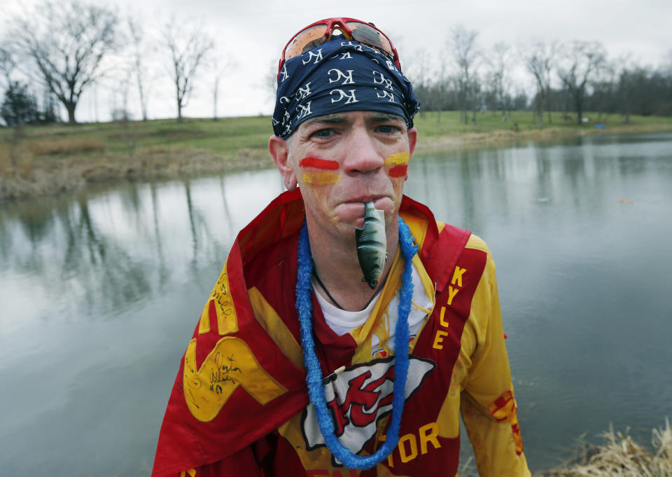 Kansas City Chiefs fan Ty Rowton, known as XFactor, exits the water with a toy fish in his mouth after takeing a Plunge for Landon in a farm pond near Bonner Springs, Kan., Friday, April 4, 2014. A 5-month-old boy's battle with cancer has inspired hundreds to jump into cold bodies of water, from a local golf course pond to the Gulf of Mexico and even the Potomac River in Washington, D.C. (AP Photo/Orlin Wagner)