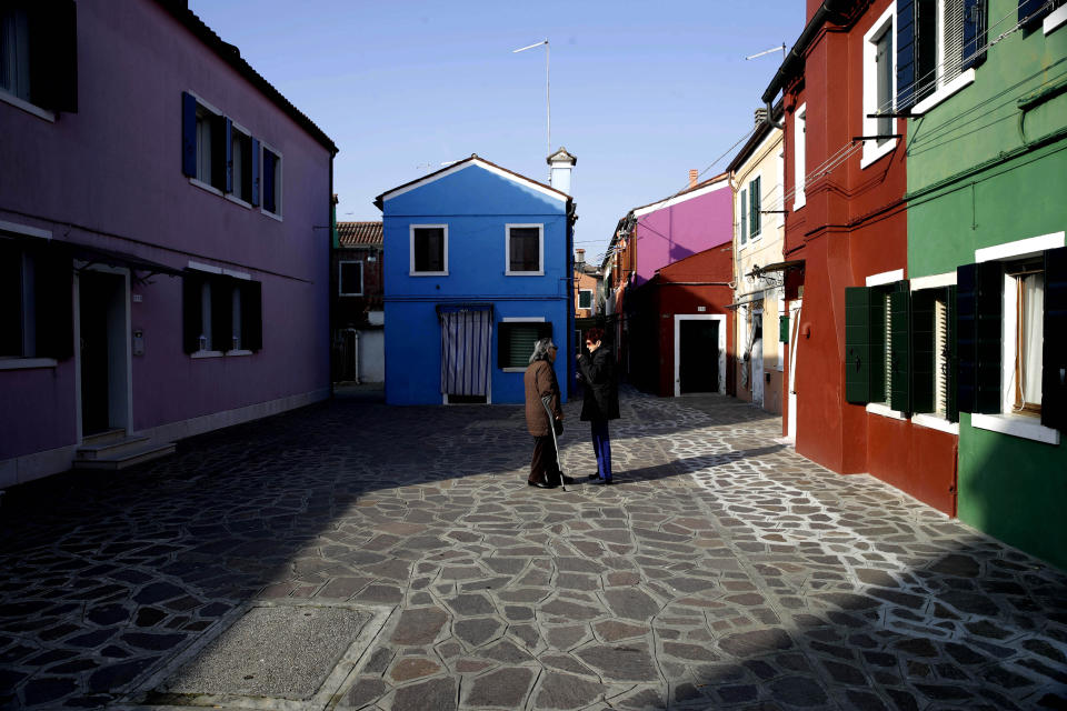 In this image taken on Thursday, Jan. 16, 2020, two women stalk in a small square of the Burano island, Italy. The Venetian island of Burano's legacy as a fishing village remains the source of its charms: the small colorful fishermen's cottages, traditional butter cookies that were the fishermen's sustenance at sea and delicate lace still stitched by women in their homes. As the island's population dwindles, echoing that of Venice itself, so too are the numbers of skilled artisans and tradespeople who have kept the traditions and economy alive. (AP Photo/Luca Bruno)