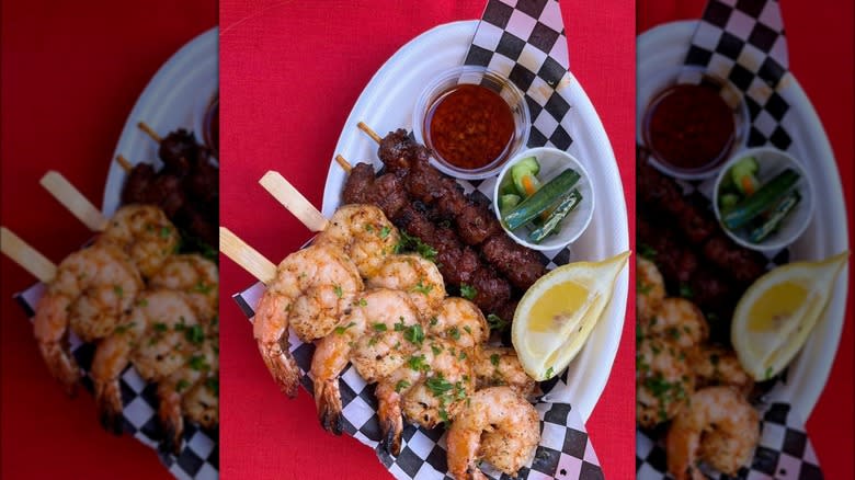 Barbecue shrimp and pork skewers against red background