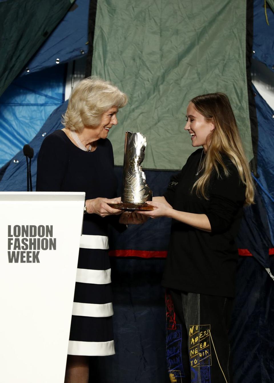 london, england   february 19 camilla, duchess of cornwall c awards the queen elizabeth ii award for british design to designer bethany williams r at the bethany williams show during london fashion week february 2019 at the bfc show space on february 19, 2019 in london, england photo by john phillipsbfcgetty images