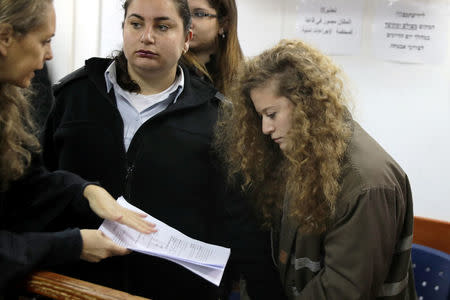 Palestinian teen Ahed Tamimi (R) looks at a document handed to her by lawyer Gaby Lasky at the military courtroom at Ofer Prison, near the West Bank city of Ramallah, February 13, 2018. REUTERS/Ammar Awad