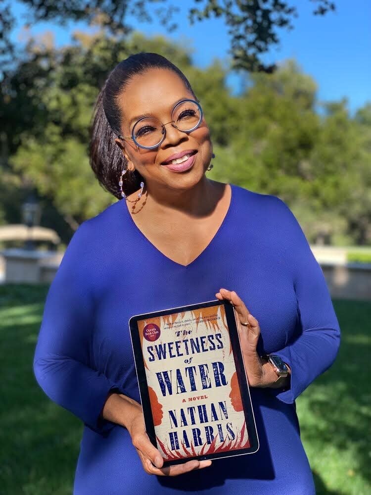 Oprah Winfrey poses for a photo with an iPad, displaying the cover image for her Oprah's Book Club selection "The Sweetness of Water" by Nathan Harris. The 29-year-old Harris, whose book comes out Tuesday, has said he wanted to show what it was like in the South after slaves were emancipated. A discussion between Winfrey and Harris will air July 23 on Apple TV+. (Harpo, Inc. via AP)