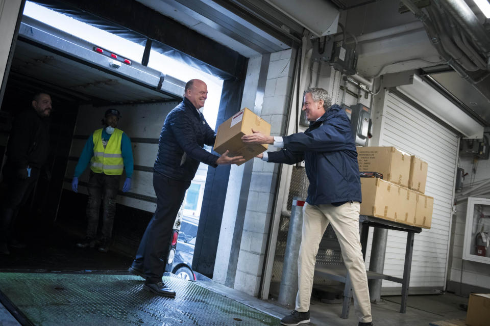 In this March 28, 2020 photo provided by the New York City Mayoral Photography Office, NYC Mayor Bill de Blasio helps load a carton containing some of 250,000 face masks into a truck on a loading dock at U.N. headquarters. The U.N. donated the masks for New York City's fight against the coronavirus. (Ed Reed/Mayoral Photography Office via AP)