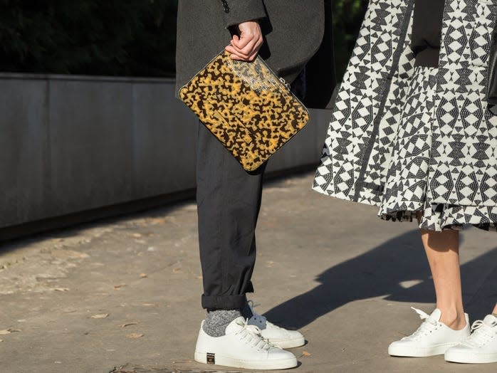 man holding a patterned envelope clutch and a woman carrying a larger black back talking on the sidewalk together