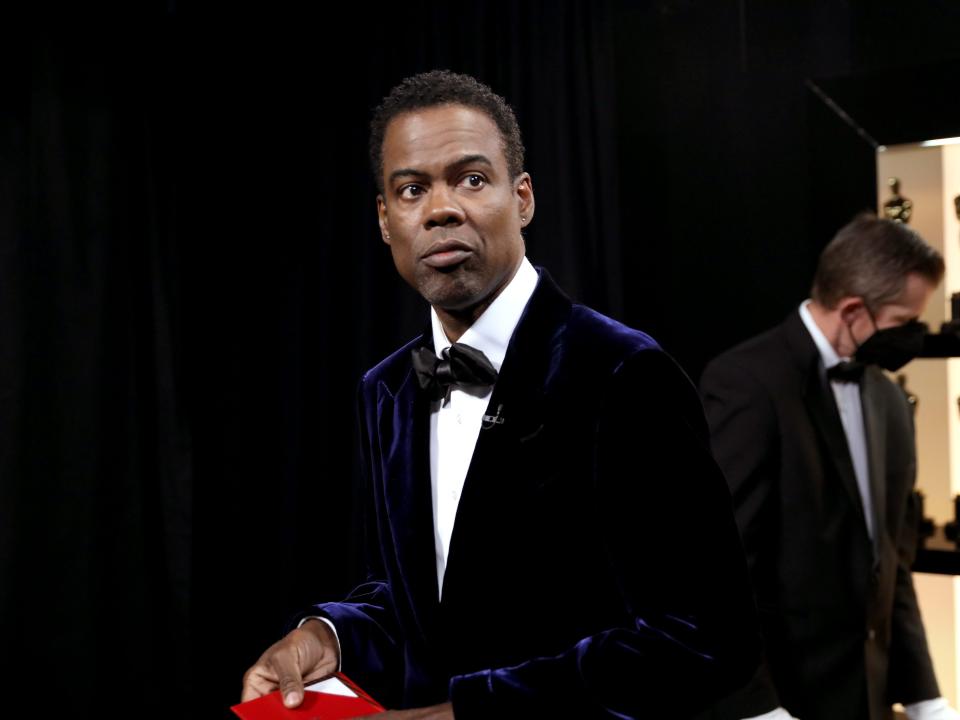 An image of Chris Rock wearing a tuxedo, carrying a red envelope