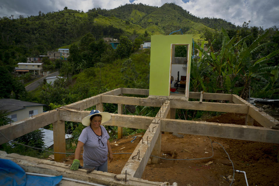 FILE - In this Sept. 8, 2018 file photo, Alma Morales Rosario poses for a portrait between the beams of her home being rebuilt after it was destroyed by Hurricane Maria a year earlier in the San Lorenzo neighborhood of Morovis, Puerto Rico. On Friday, May 10, 2019, The Associated Press has found that stories circulating on the internet that Puerto Rico has received $91 billion from Congress for hurricane disaster relief, more than any state in the U.S, are untrue. Congress has approved $41 billion in aid for recovery efforts in the U.S. territory, but only about $11 billion of that aid has been dispersed. (AP Photo/Ramon Espinosa)