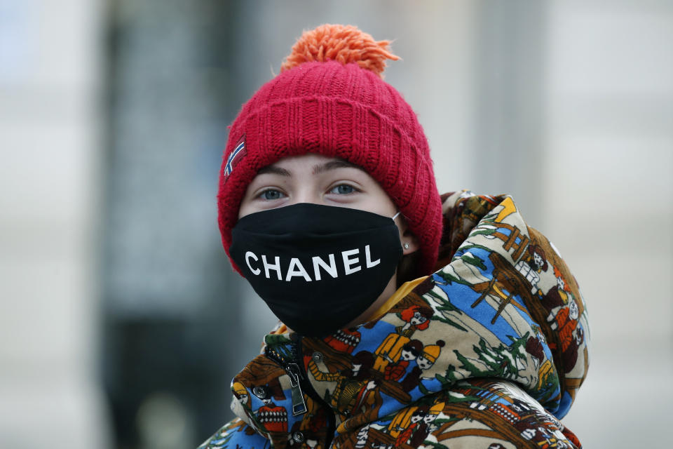 FILE - In this May 11, 2020 file photo, a woman wears a face mask on the Champs Elysee avenue in Paris. The French praised the altruism of luxury goods companies such as LVMH, Kering and Chanel for diverting their production facilities to make millions of face masks for the public during the peak of their country's coronavirus outbreak. Now, the companies that helped France avoid a dangerous shortage say they need help unloading a surplus of 20 million washable masks. (AP Photo/Francois Mori, File)