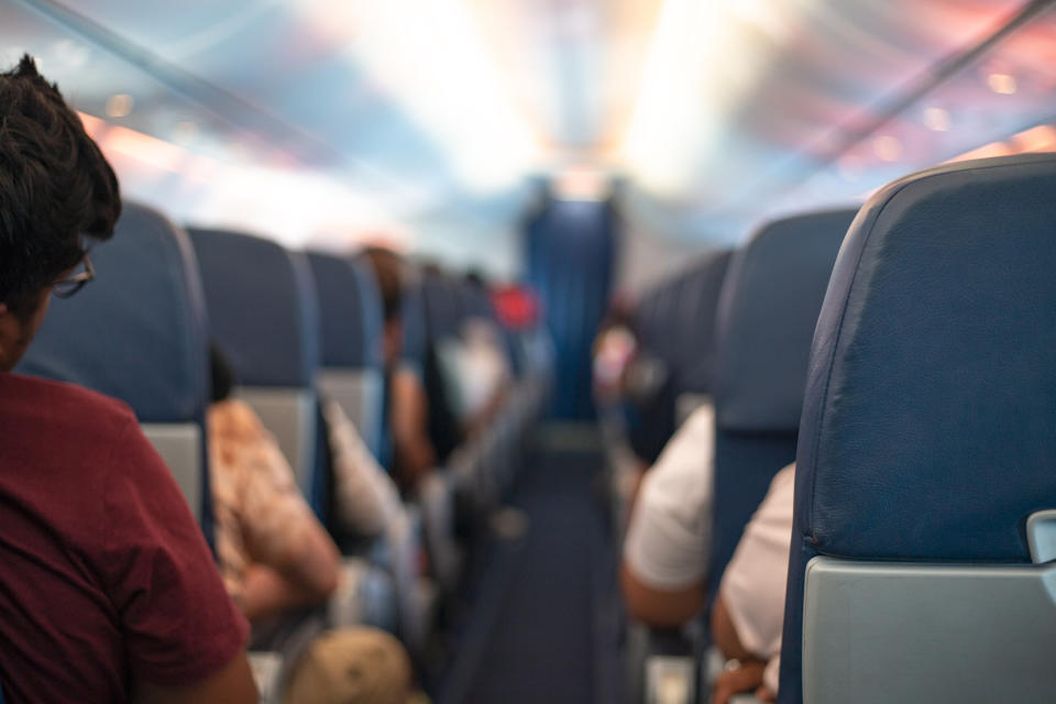 Passengers seated inside an airplane looking towards the front cabin