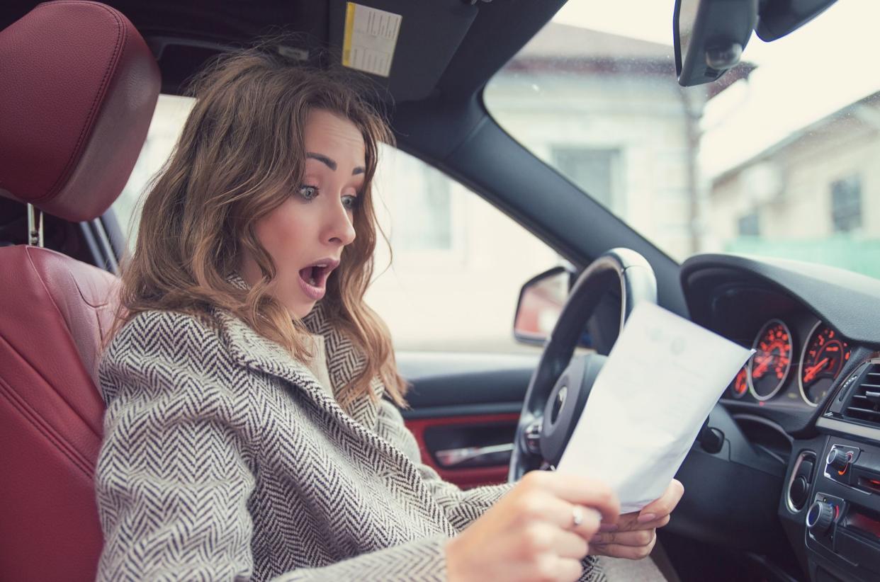 Young girl sitting inside of a car and reading fine papers, looking frustrated.