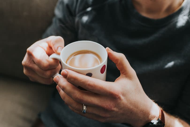 Man holding a cup of tea in two hands, in a spotty mug.