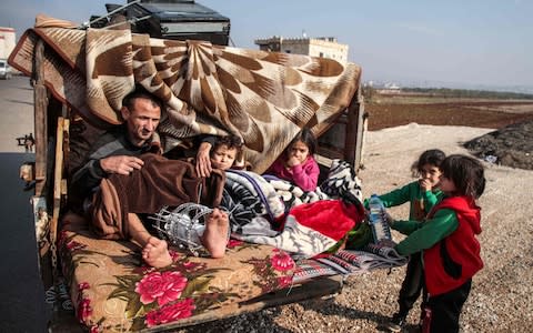 An injured man sits alongside children in the back of a truck as part of a convoy of vehicles of people from the south of Idlib province fleeing bombardment by the government and its allies on the northwestern region, - Credit: AFP