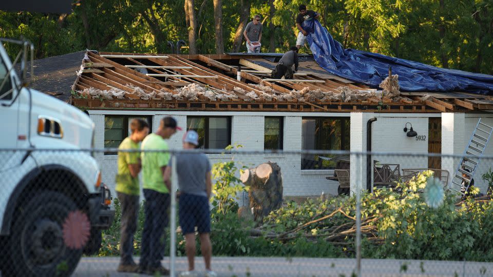 Workers put a tarp over a damaged roof after a reported tornado touched down in Johnson County, Indiana, Sunday.  - Jenna Watson/The Indianapolis Star/AP