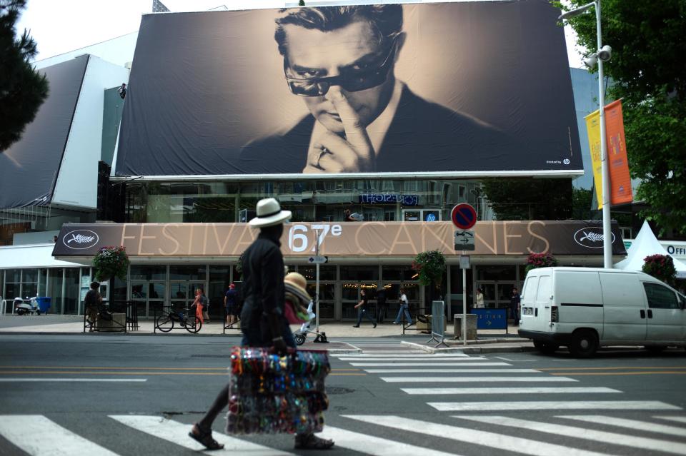 A street vendor walks past a banner depicting Marcello Mastroianni from Federico Fellini’s film 8½ on the Palais prior to the 67th international film festival, Cannes, southern France, Monday, May 12, 2014. The festival runs from May 14 to May 25. (AP Photo/Thibault Camus)