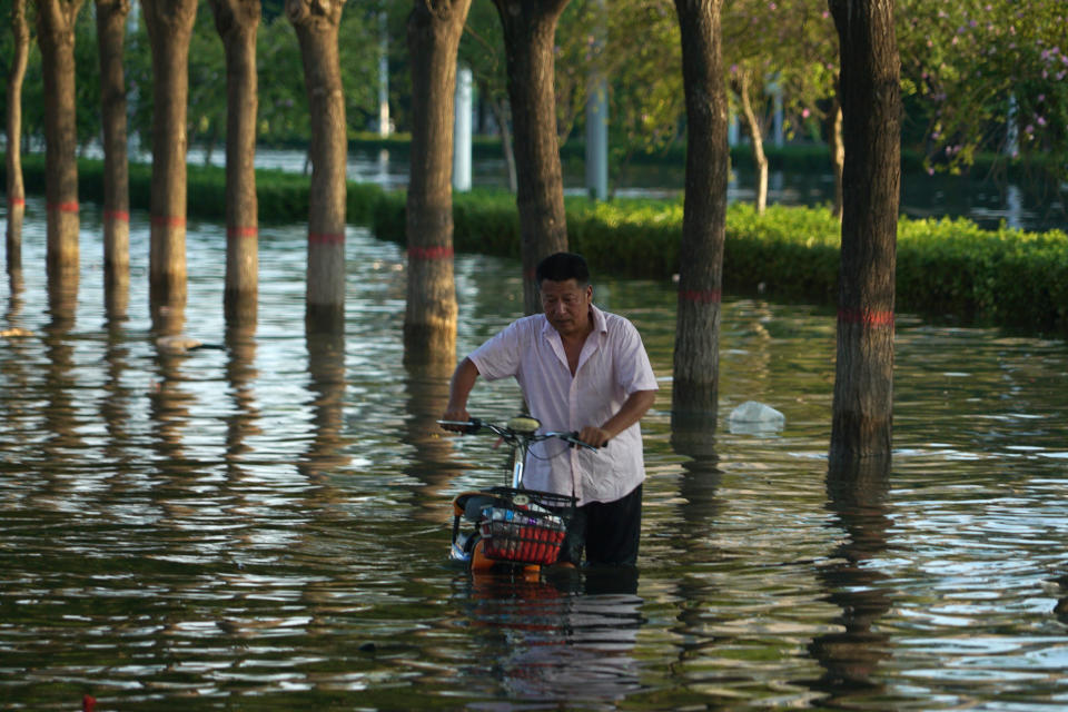 A man pushes a scooter through floodwaters in Xinxiang in central China's Henan Province, Monday, July 26, 2021. Forecasters Monday said more heavy rain is expected in central China's flood-ravaged Henan province, where the death toll continues to rise after flash floods last week that killed dozens of people. (AP Photo/Dake Kang)