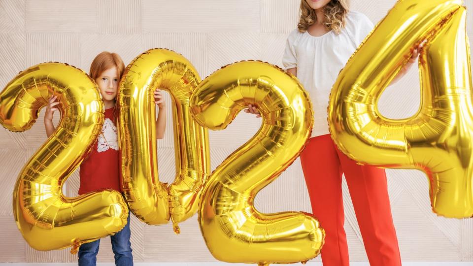 beautiful happy mother and daughter having fun decorating home for christmas, holding giant balloons shaped as numbers 2024 representing the upcoming new year