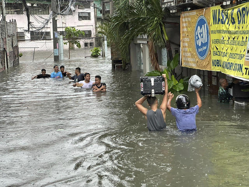 People wade through a flooded street following monsoon rains worsened by offshore typhoon Gaemi on Wednesday, July 24, 2024, in Manila, Philippines. (AP Photo/Joeal Capulitan)