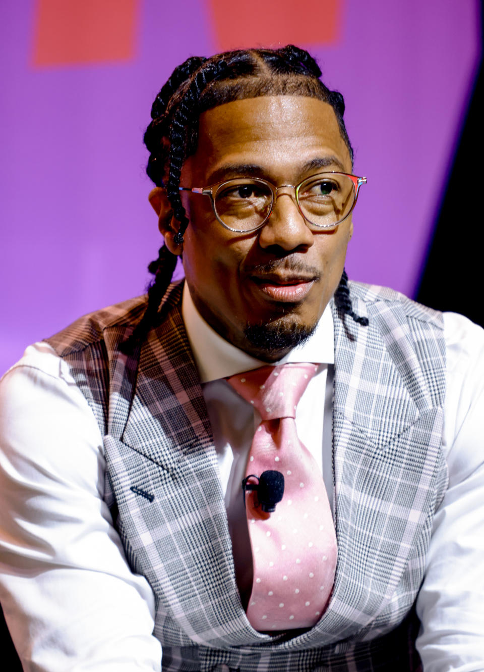 Nick Cannon in a checkered vest and pink polka dot tie speaks at an event