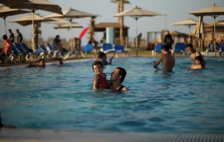 A Palestinian man holding his daughter swims in a pool as they enjoy the warm weather with their family at the Blue Beach Resort in Gaza July 30, 2015. REUTERS/Mohammed Salem