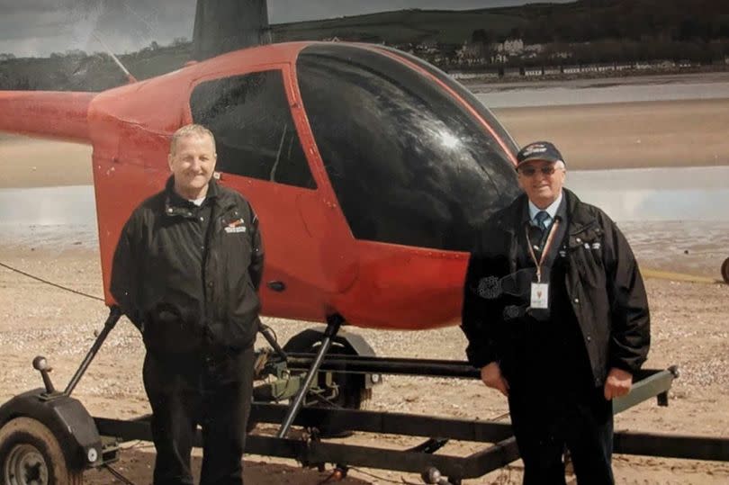 Two men stood in front of a small helicopter