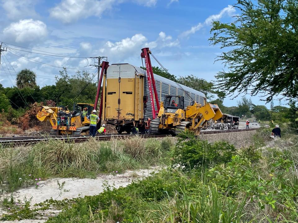 Workers crawl beneath freight train car and lift with machinery to set it on tracks May 20, 2022. Eght card derailed Thursday evening, with five of them toppling over.