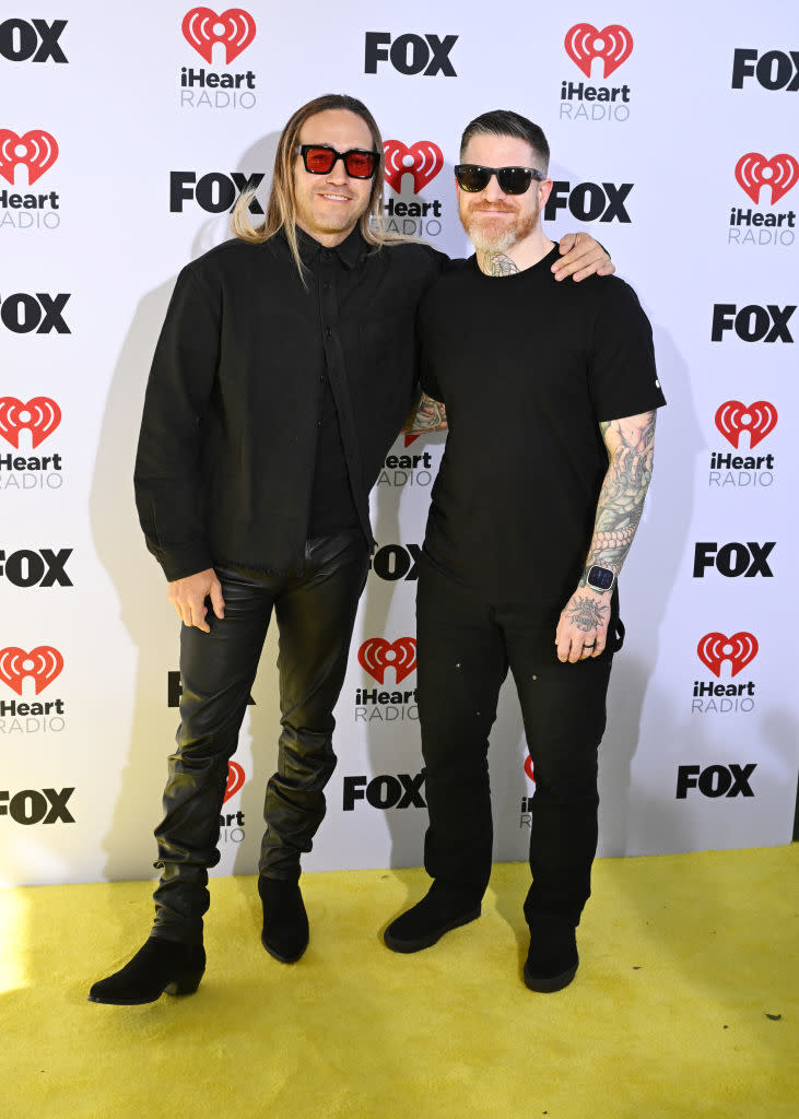 Two men at an event wearing black outfits and sunglasses, posing for the camera