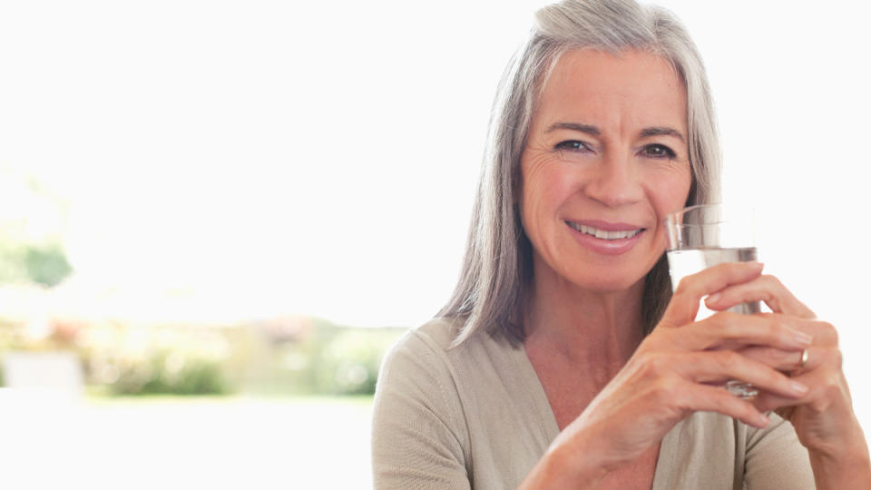 A woman with grey hair smiling as she holds a glass of water