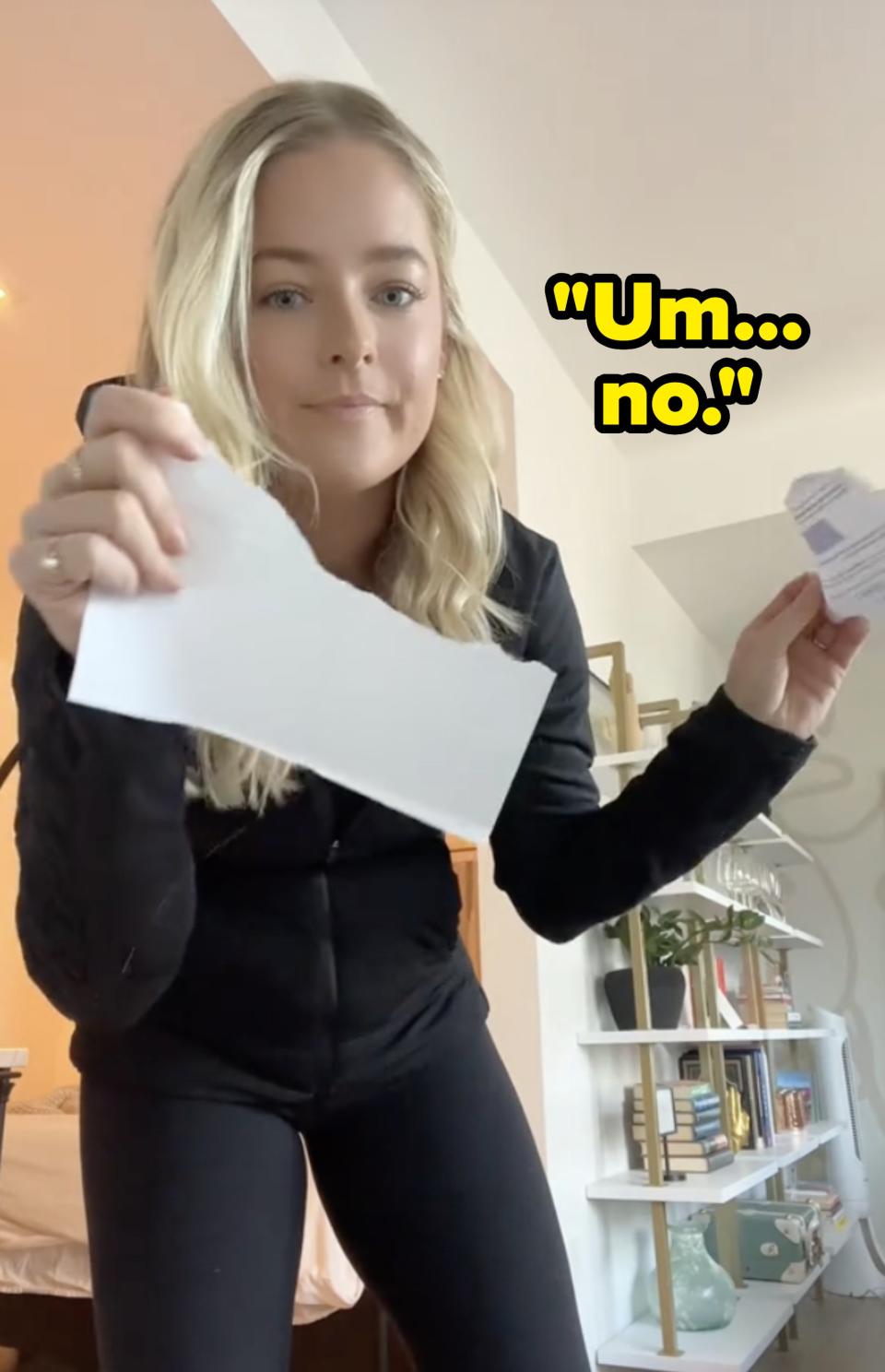 Woman in black outfit holding out a piece of paper towards the camera
