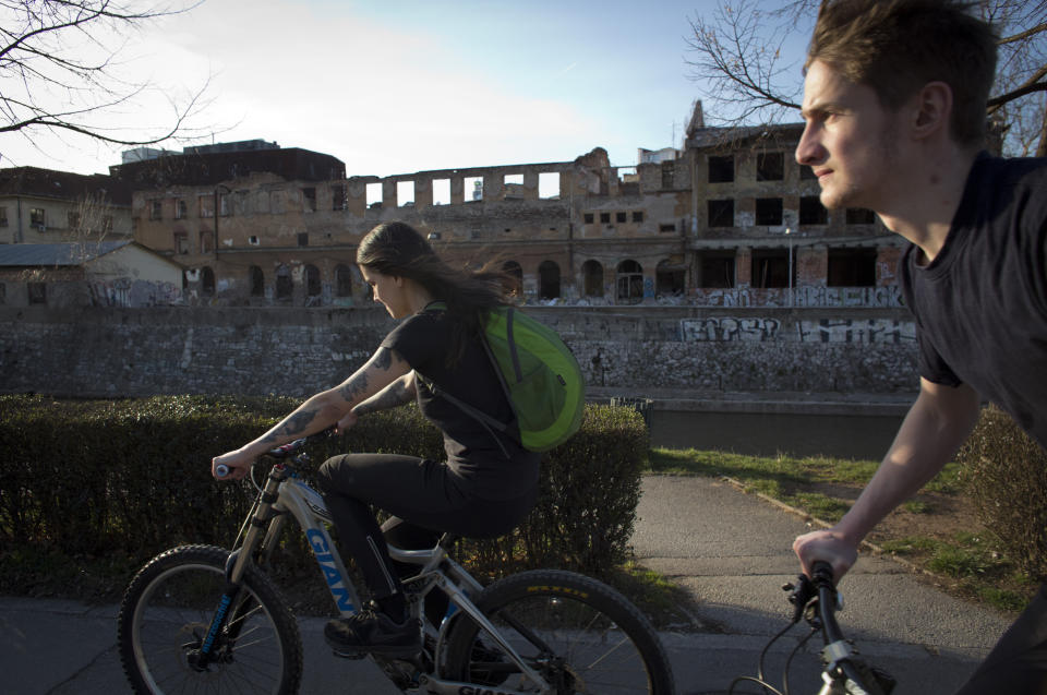In this Sunday, March 17, 2019 photo, cyclists ride past war damaged buildings in Sarajevo, Bosnia-Herzegovina. Nearly a quarter of a century since Bosnia's devastating war ended, former Bosnian Serb leader Radovan Karadzic is set to hear the final judgment on whether he can be held criminally responsible for unleashing a wave of murder and mistreatment by his administration's forces. United Nations appeals judges on Wednesday March 20, 2019 will decide whether to uphold or overturn Karadzic's 2016 convictions for genocide, crimes against humanity and war crimes and his 40-year sentence. (AP Photo/Darko Bandic)