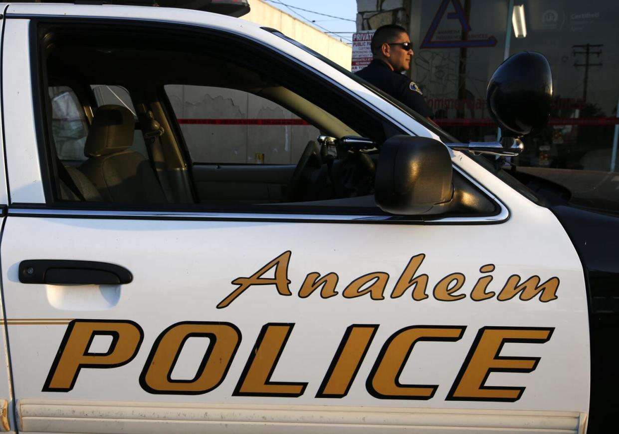 An Anaheim police officer stands besides a patrol car.