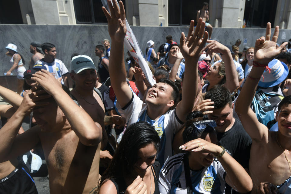 Soccer fans look up for water thrown by neighbors in Buenos Aires, Argentina Tuesday, Dec. 20, 2022. Fans descended into the streets of the capital eager to catch a glimpse of the open-top bus carrying the Argentine national soccer team that won the World Cup final. (AP Photo/Mario De Fina)