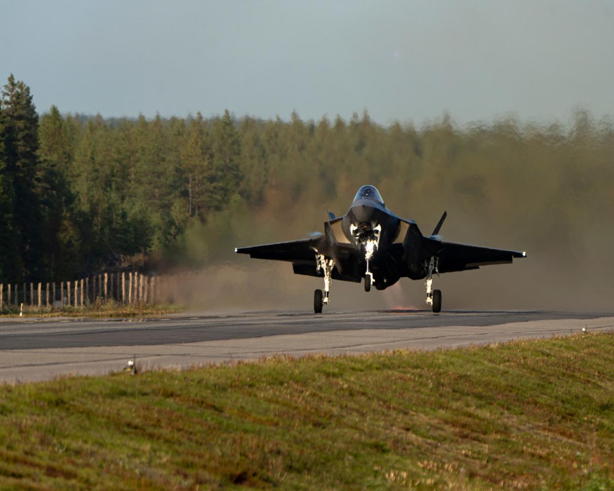 A US Air Force F-35 fighter jet lands on a highway with trees in the background.