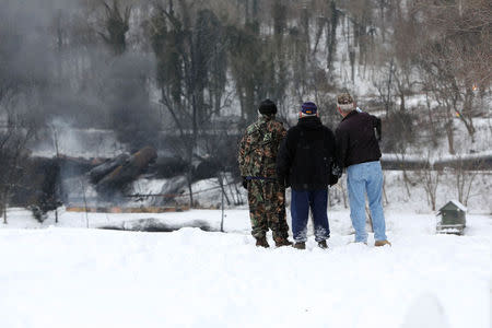 From left, Anthony "Buzz" Fish, 71, Lewis F. Fish 74, and Tom Graham, 73, all of Boomer, West Virginia, watch as a CSX Corp train continues to smolder a day after derailing in Mount Carbon, West Virginia, Tuesday, February 17, 2015. REUTERS/Marcus Constantino