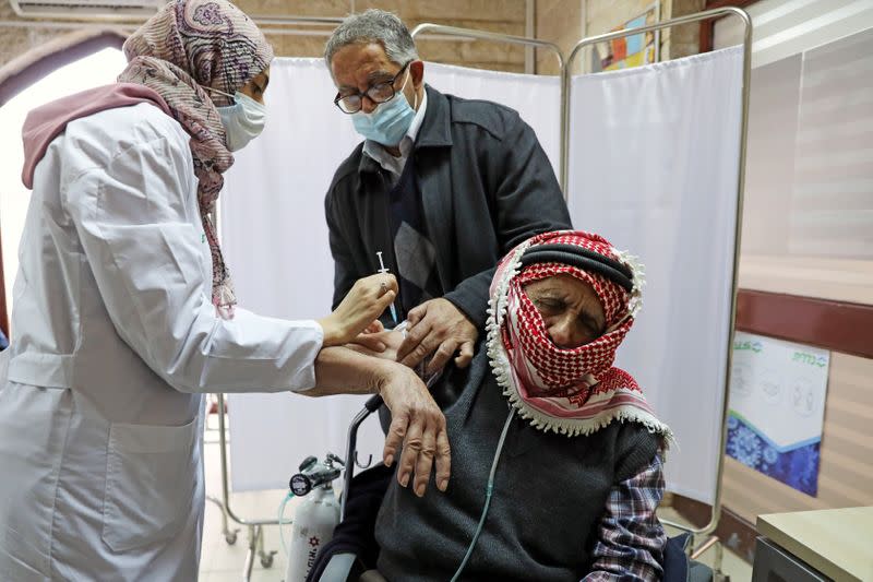 A Palestinian man is helped by his son as he receives a vaccination against the coronavirus disease (COVID-19) as Israel continues its national vaccination drive, in East Jerusalem