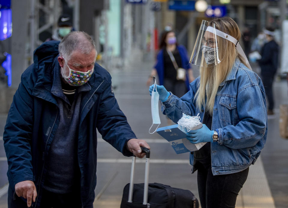 FILE - In this April 27, 2020 file photo, a woman working for the regional public transport company offers a face mask to an elderly man in the main train station in Frankfurt, Germany. More than 50,000 people have died after contracting COVID-19 in Germany, a number that has risen swiftly over recent weeks as the country has struggled to bring down infection figures. (AP Photo/Michael Probst, File)