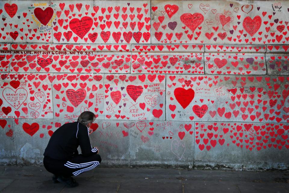 <p>A man paints a heart on the National Covid Memorial Wall in London</p> (AP)