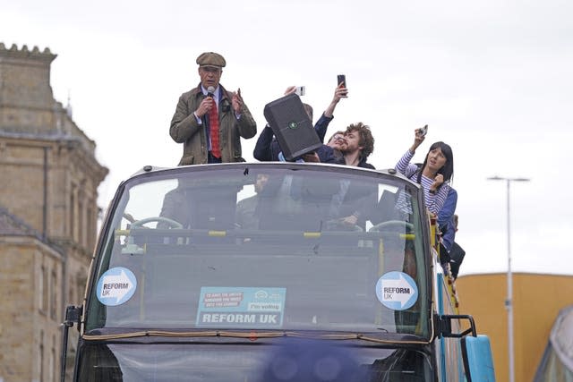 Open top bus carrying a group of people including Nigel Farage, in a tweed flat cap and jacket, who speaks into a loudspeaker