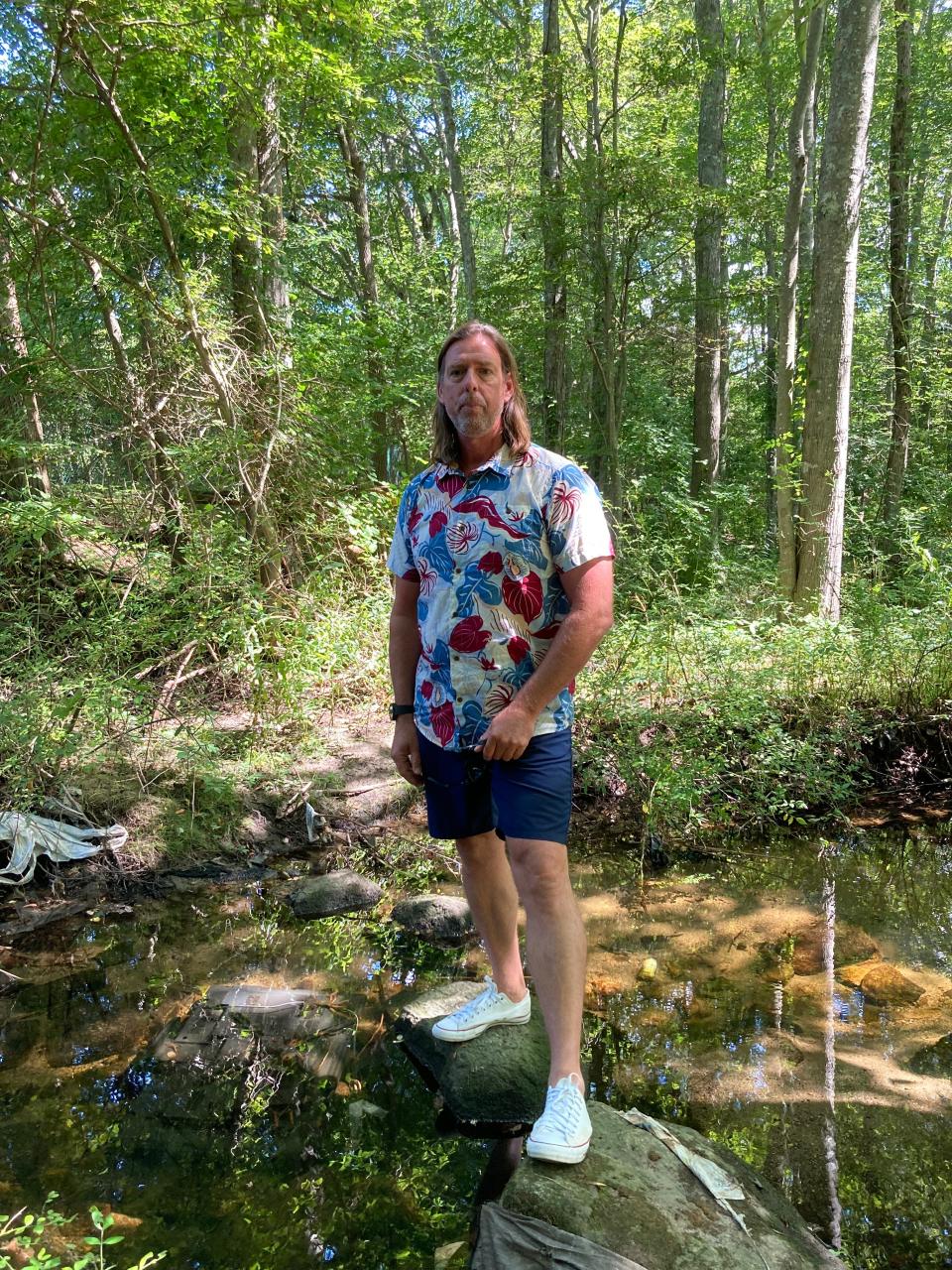 Buttonwood to Bay Project Manager Daniel Goulart stands on the rocks at the beginning of Buttonwood Brook where trash has been dumped, with the Hidden Brook apartments nearby.