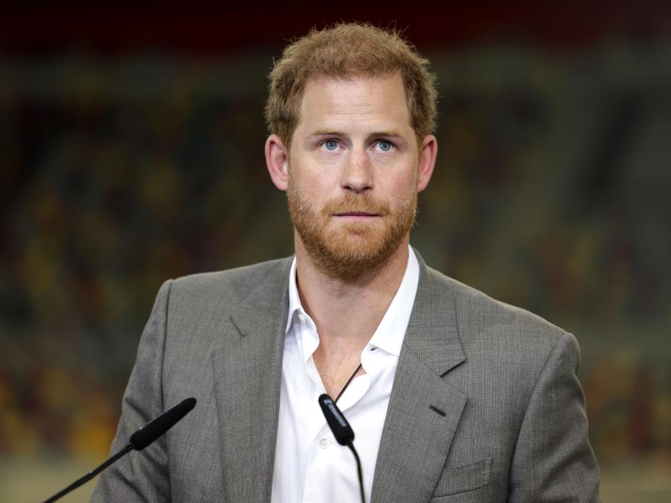 Prince Harry speaks into a microphone in a gray jacket and a white shirt