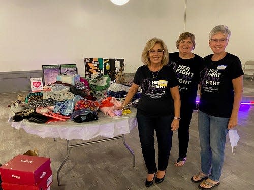 Members of the Domestic Violence Committee, Jan Bicknell, Lynn Corley and Patti Becker stand beside the table filled with donations from generous members of the Lincoln Woman’s Club in Lincoln, Illinois.