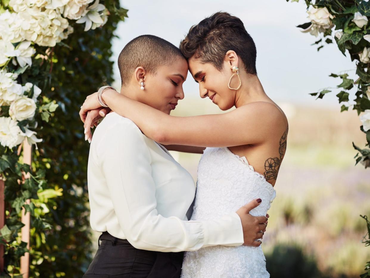 A couple touch their foreheads together under their wedding arch.