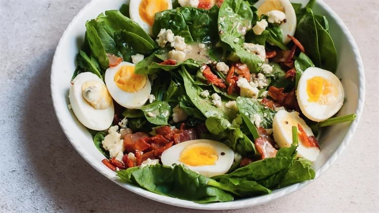 Warm spinach salad in white bowl