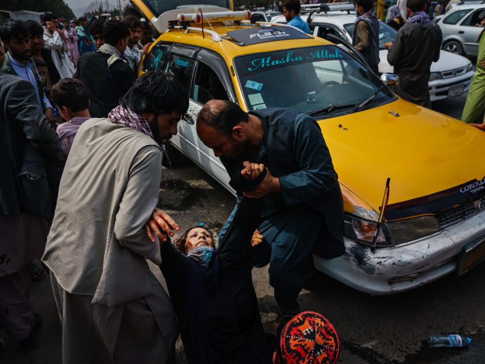 Men try to help a wounded woman after Taliban fighters maintained crowd control with lethal weapons