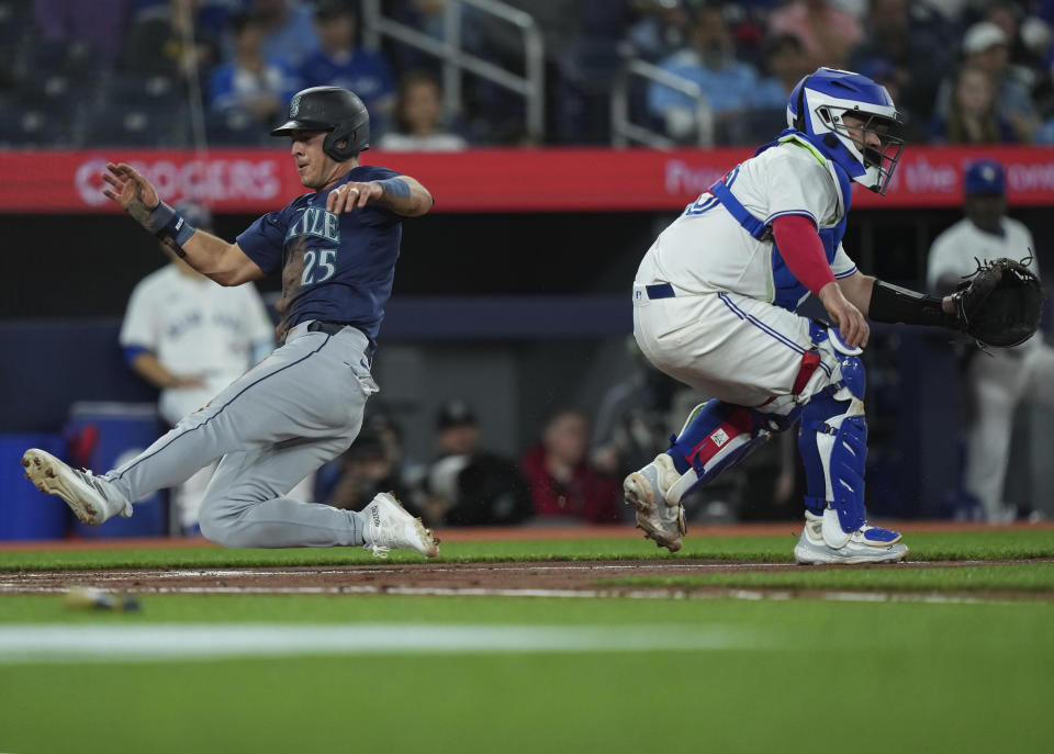 Seattle Mariners' Dylan Moore (25) score a run past Toronto Blue Jays catcher Alejandro Kirk (30) during the third inning of a baseball game in Toronto, Wednesday, April 10, 2024. (Nathan Denette/The Canadian Press via AP)